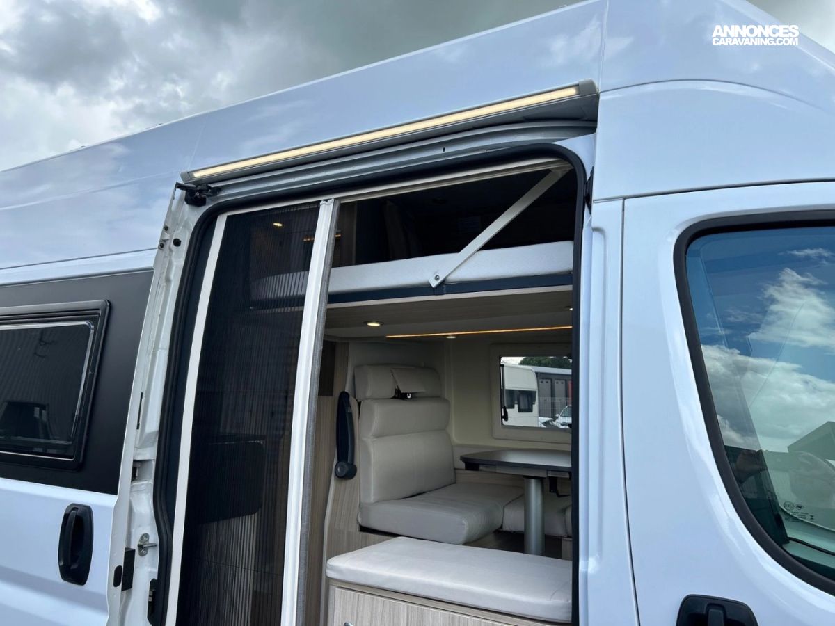 Porte coulissante ouverte du van aménagé PyjaVan avec moustiquaire, coin repas et lit en hauteur