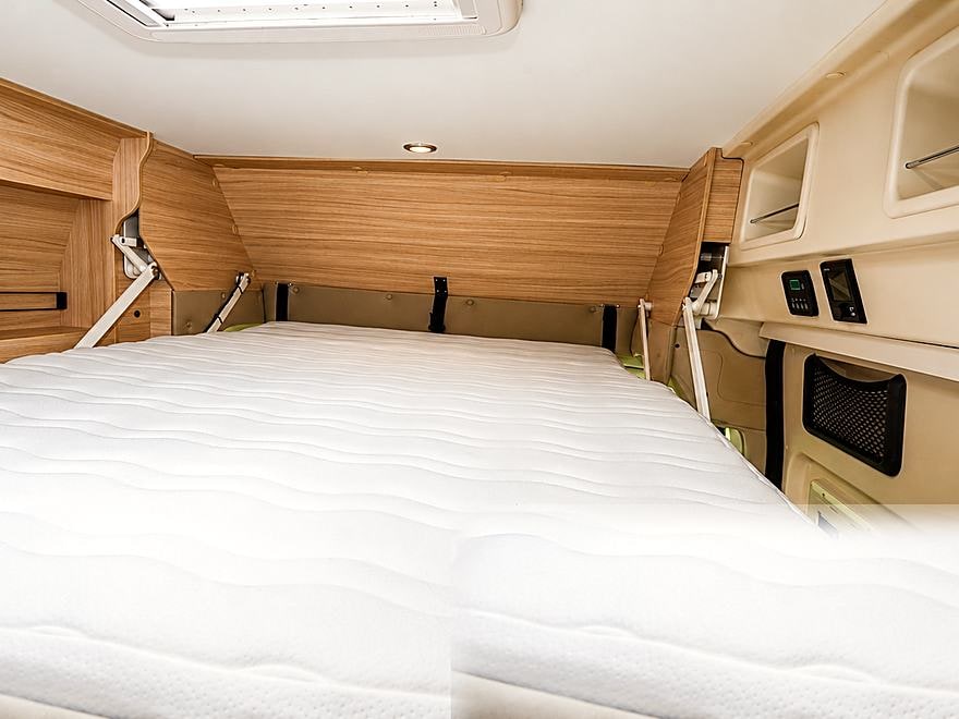 Lit double à l'arrière du van, matelas et rangements en bois clair
